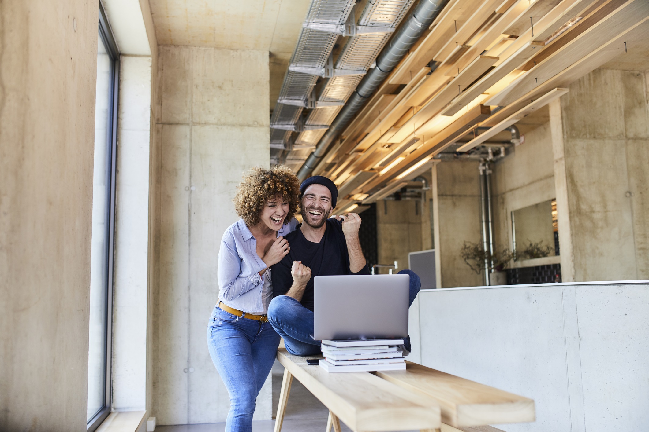 Eine Frau und ein Mann stehen in einem loft-artigen Wohnzimmer vor dem Laptop.