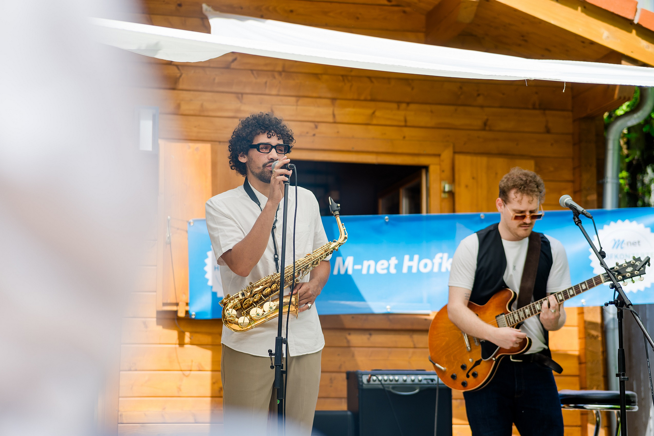 Zwei Sänger stehen auf einer kleinen Bühne im Hinterhof bei einem M-net Hofkonzert.